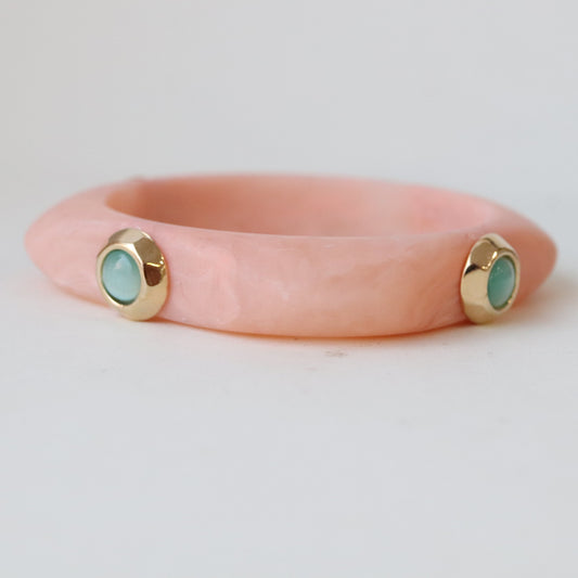 Pulsera de resina color rosa con detalles dorados y piedras turquesas, estilo moderno y elegante.
