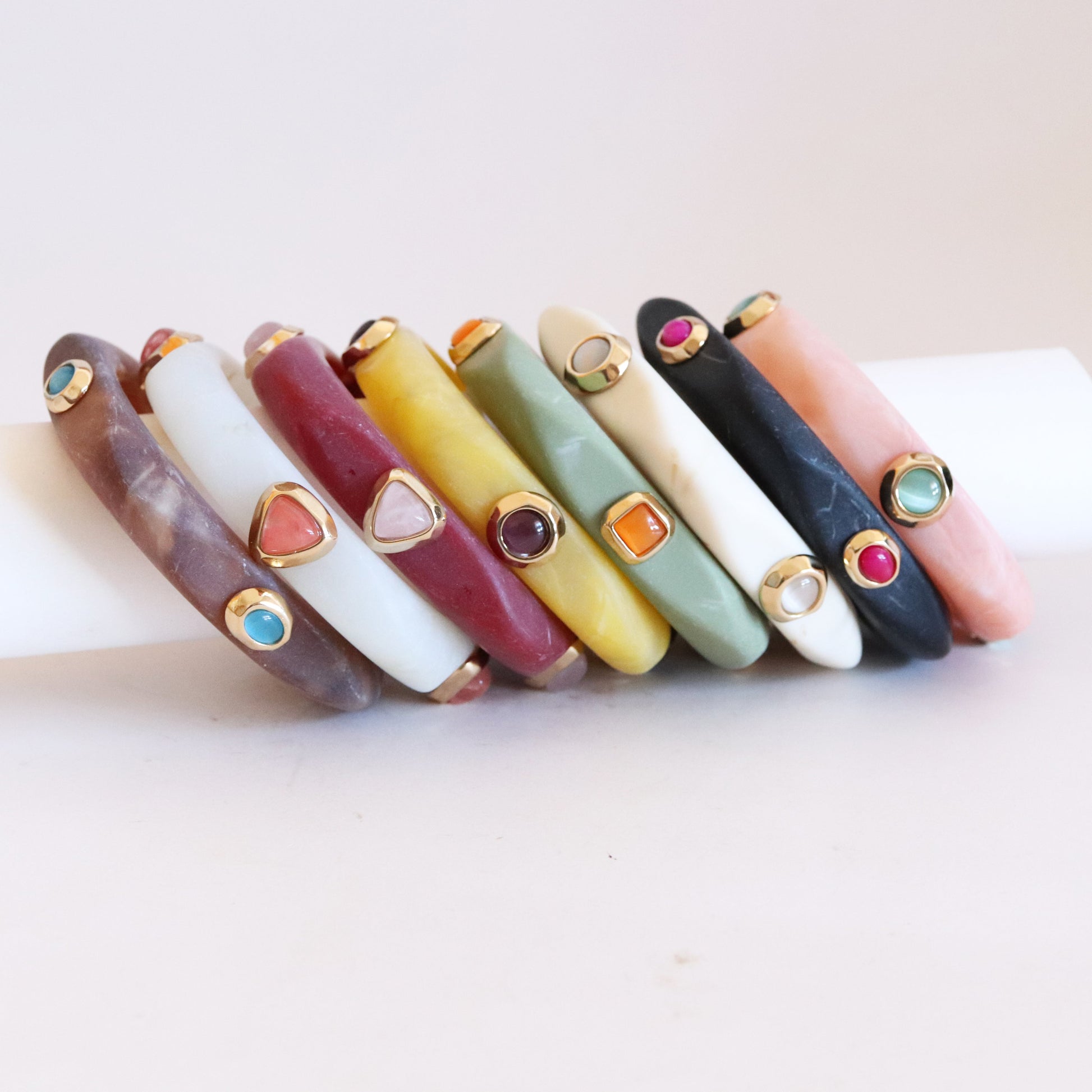 Pulseras de resina en tonos variados con detalles dorados y piedras preciosas, estilo moderno y colorido.