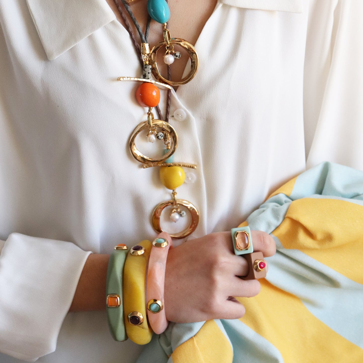 Collar dorado con piedras de colores, pulseras pastel y anillo con detalles brillantes, estilo moderno y vibrante.