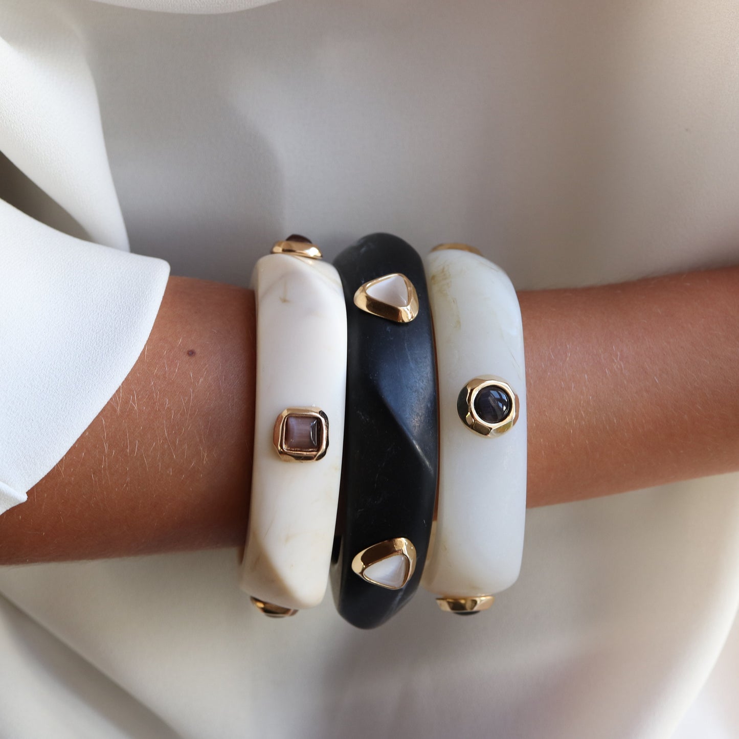 Pulseras de resina blanca y negra con detalles dorados y piedras decorativas, estilo elegante y moderno.