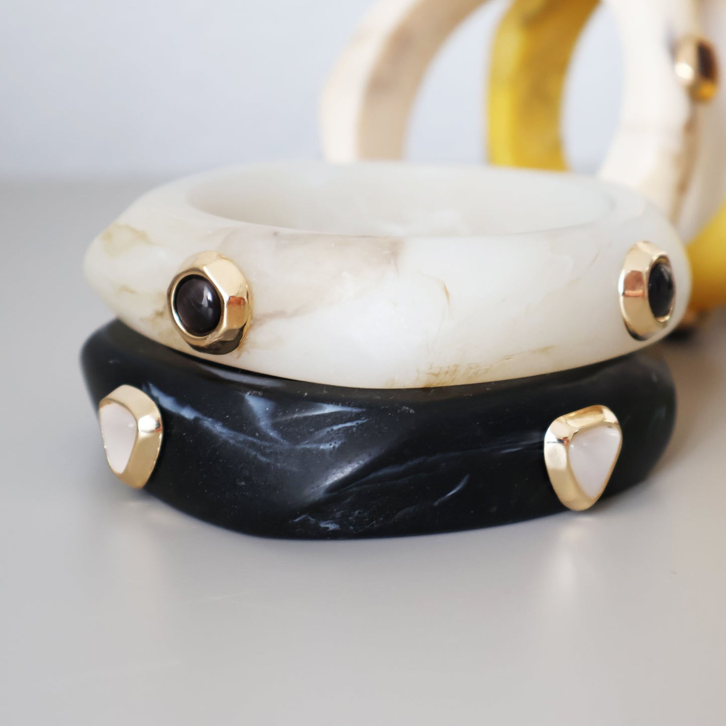 Brazaletes de resina blanca y negra con detalles dorados y piedras, estilo moderno y elegante.