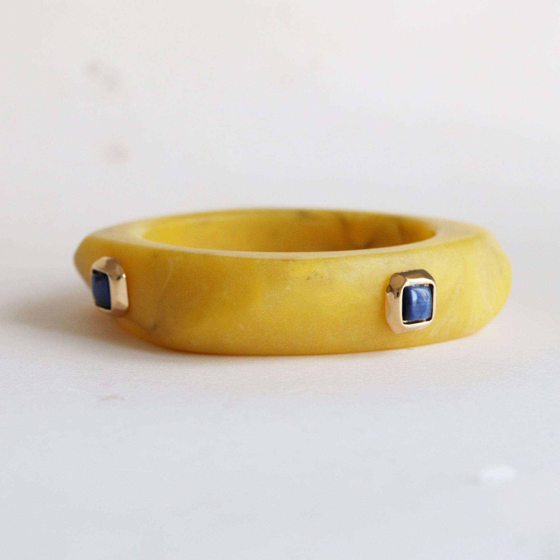 Brazalete amarillo de resina con detalles en oro y piedras azules, estilo moderno y elegante.