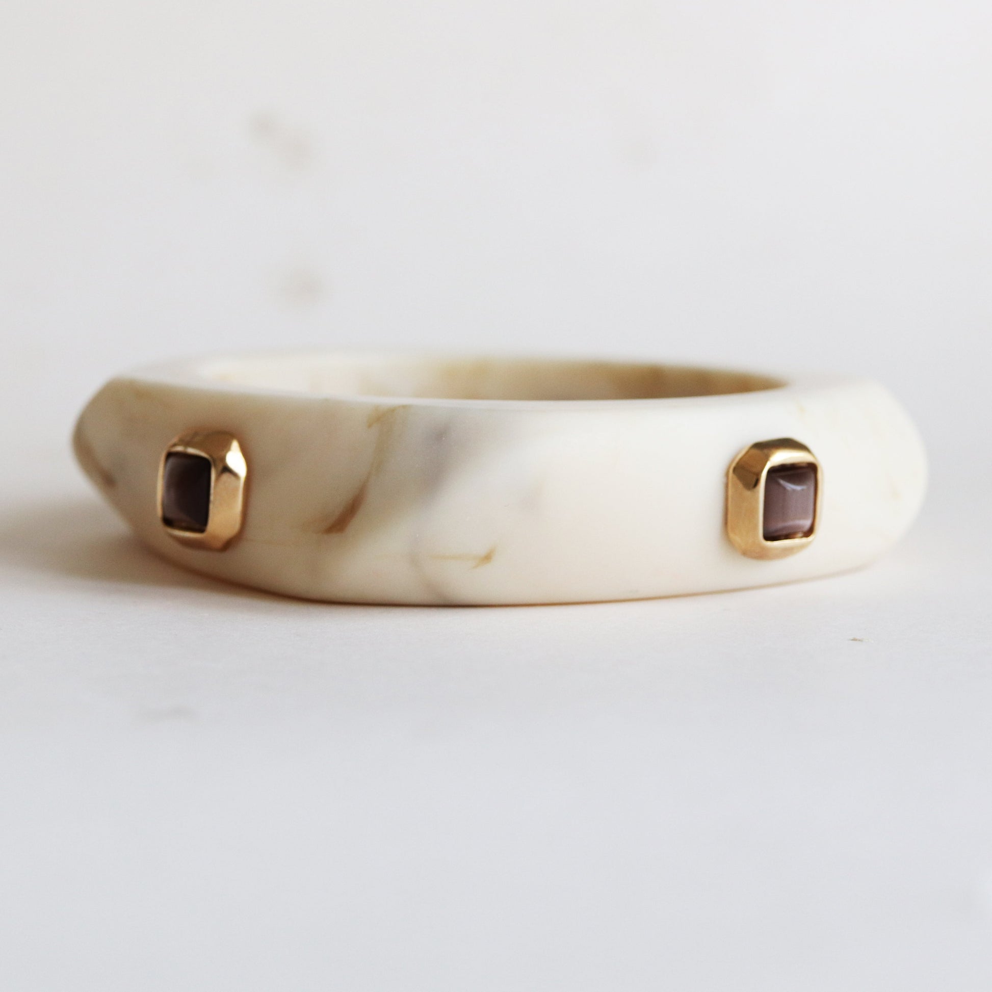 Pulsera de resina blanca con detalles en oro y gemas marrones, diseño moderno y elegante.