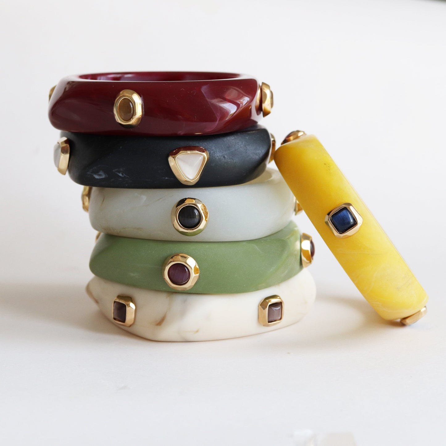 Pulseras apiladas en tonos rojo, negro, gris, verde, amarillo y blanco, con detalles dorados y piedras decorativas.