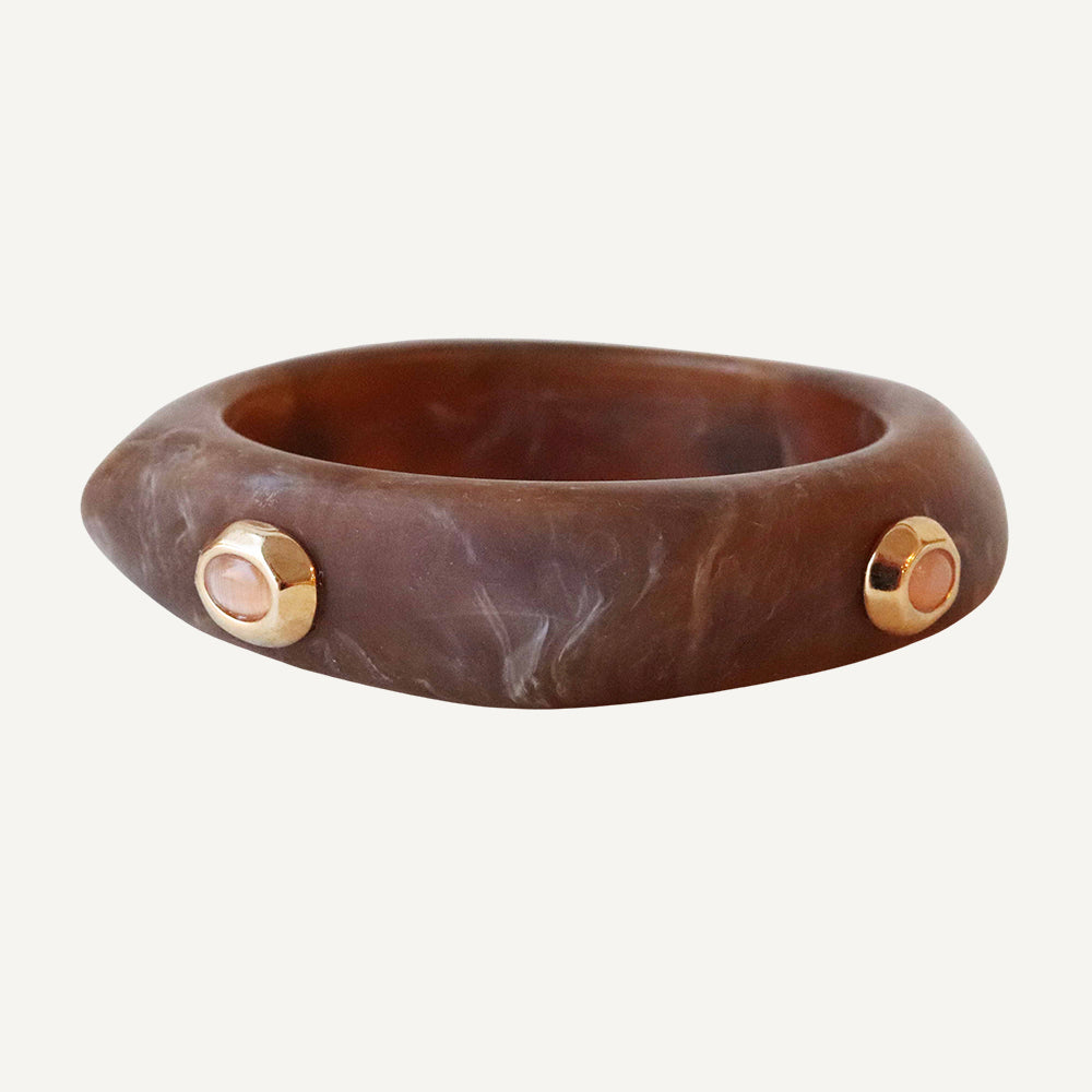Brazalete de resina marrón con detalles dorados y piedras rosas, estilo moderno y elegante.