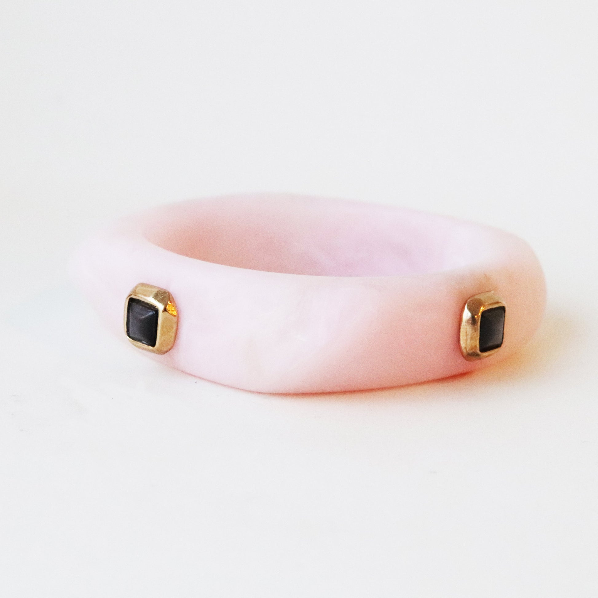 Pulsera rosa de resina con detalles en oro y gemas negras, estilo moderno y elegante.