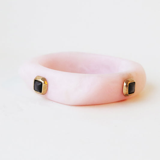 Pulsera rosa de resina con detalles en oro y gemas negras, estilo moderno y elegante.