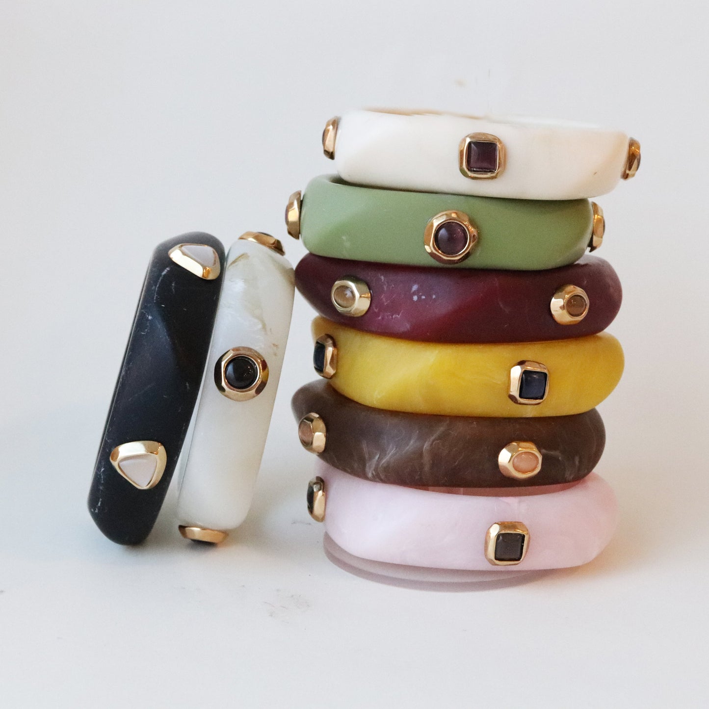 Pulseras de resina en tonos variados (verde, negro, púrpura, amarillo, marrón, rosa) con detalles dorados y gemas.
