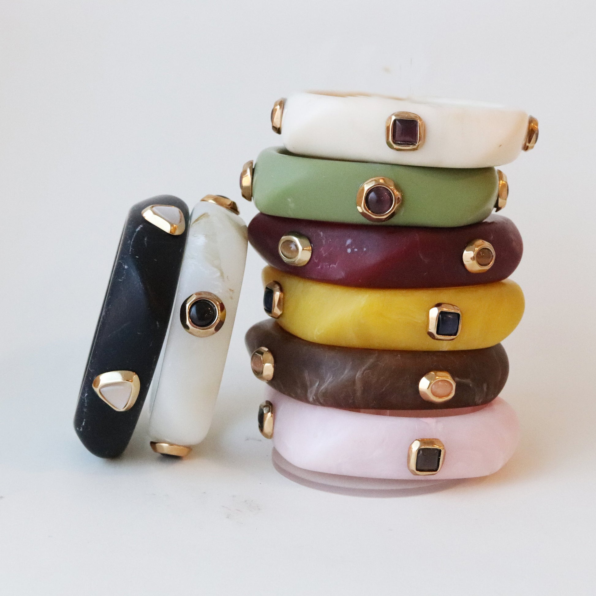 Pulseras de resina en tonos variados (verde, negro, púrpura, amarillo, marrón, rosa) con detalles dorados y gemas.