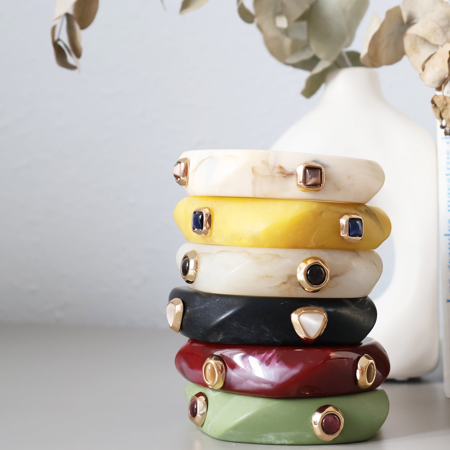 Pulseras de resina en tonos amarillo, blanco, negro, verde y rojo, con detalles dorados y piedras de colores.