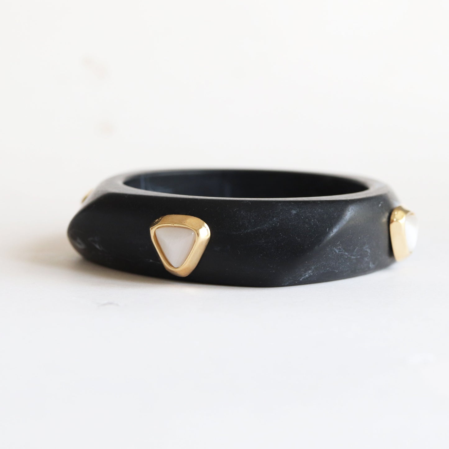 Pulsera de resina negra con detalles dorados y gemas blancas, estilo moderno y elegante.