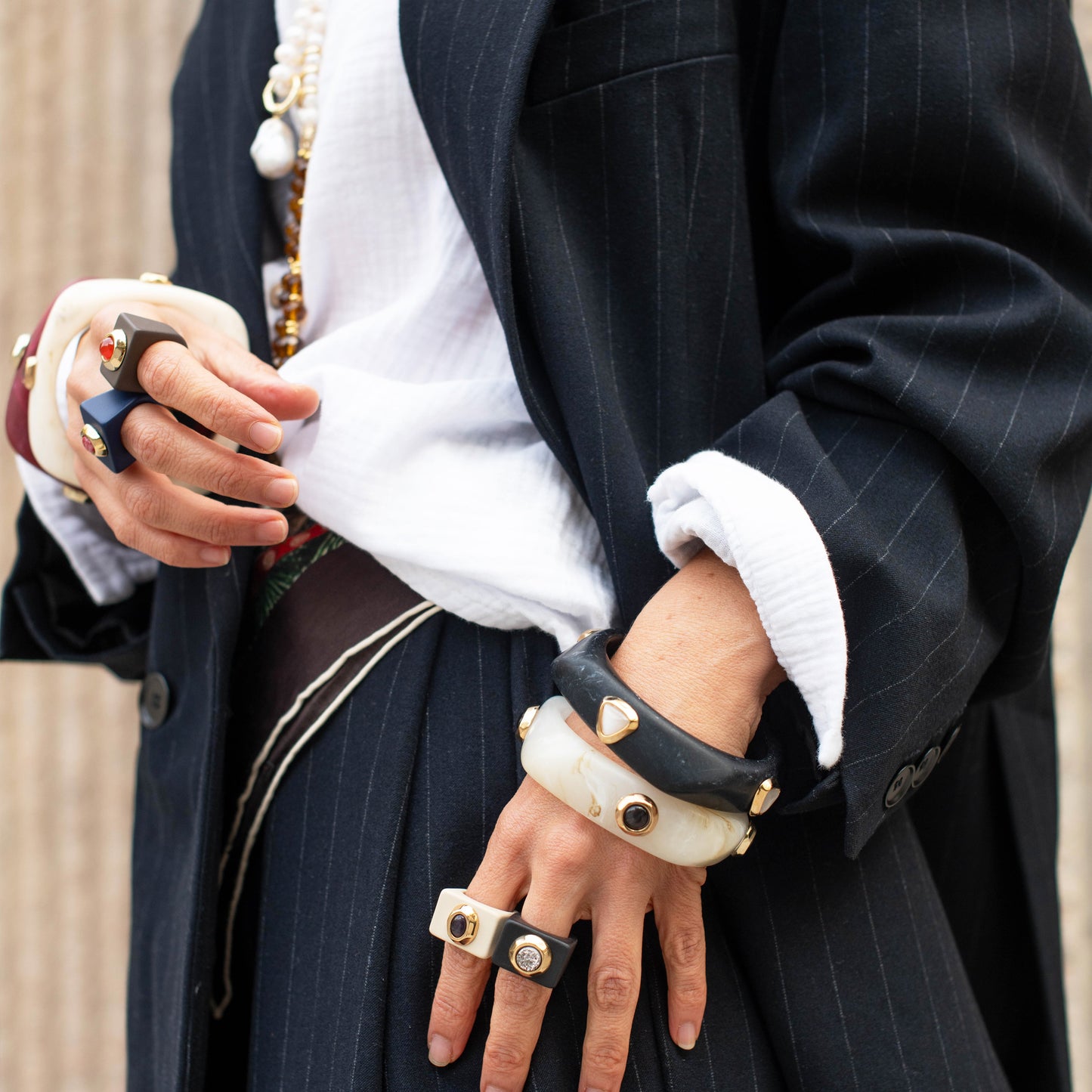 Conjunto de pulseras negras y blancas con detalles dorados, estilo elegante y moderno, sobre chaqueta a rayas.