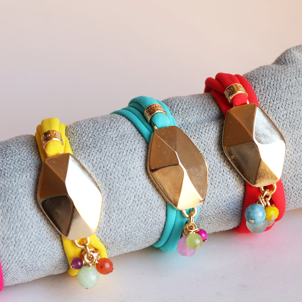 Pulseras de colores amarillo, azul y rojo con detalles dorados y cuentas de piedras, estilo moderno y vibrante.