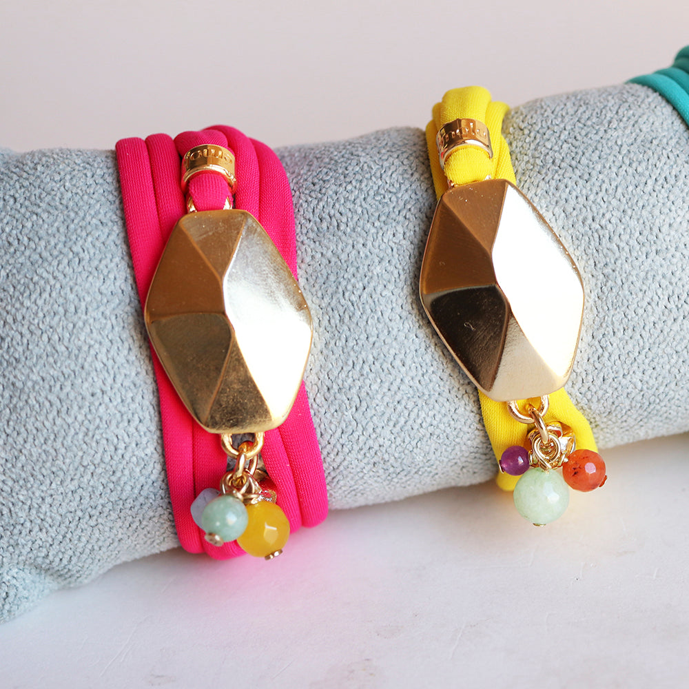 Pulseras de tela fucsia y amarilla con detalle dorado y piedras de colores, estilo moderno y vibrante.
