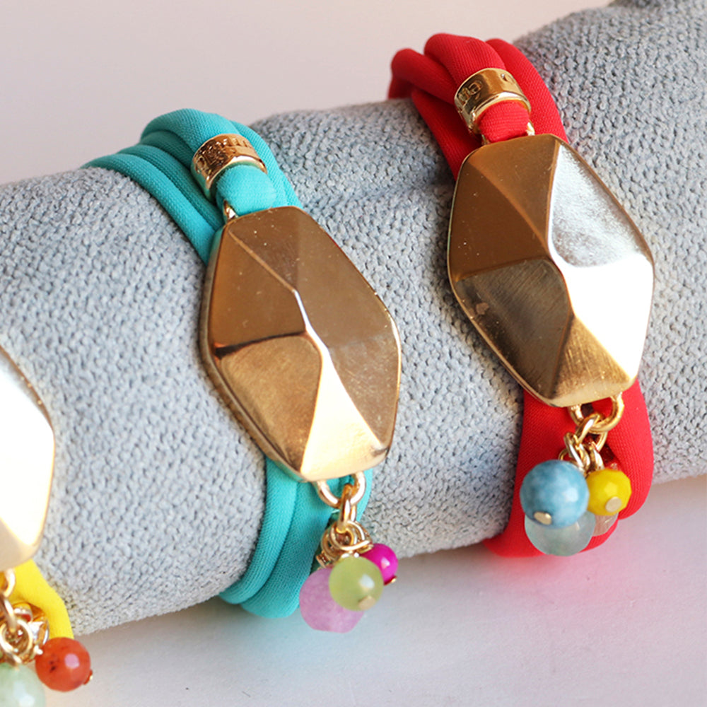 Pulsera de tela color aqua, rojo y amarillo con adornos dorados y cuentas de colores, estilo moderno y vibrante.