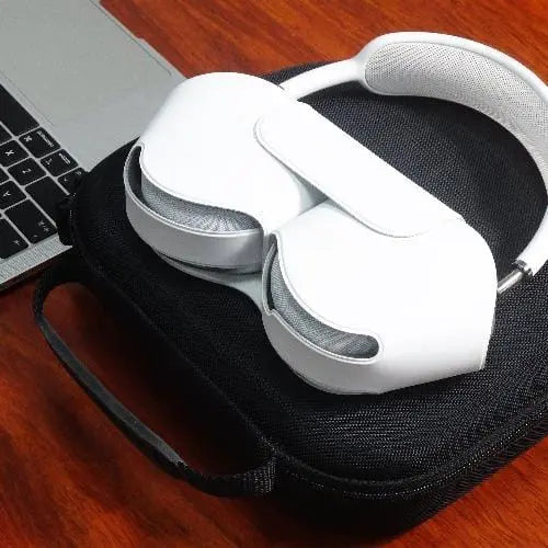 White AirPods Max headphones resting on a black, hard-shell zippered travel carry case next to a laptop.