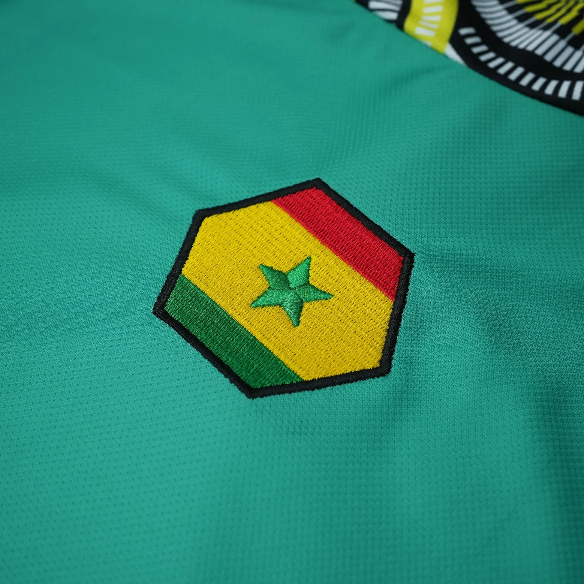 Maillot vert VO7 avec blason hexagonal brodé aux couleurs du Sénégal et détails graphiques sur l'épaule.