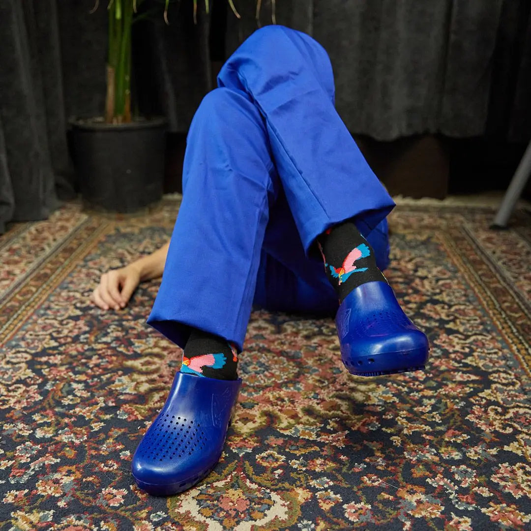 Metallic blue clog-style shoes with toe-box ventilation holes, worn with patterned socks and blue scrub pants.