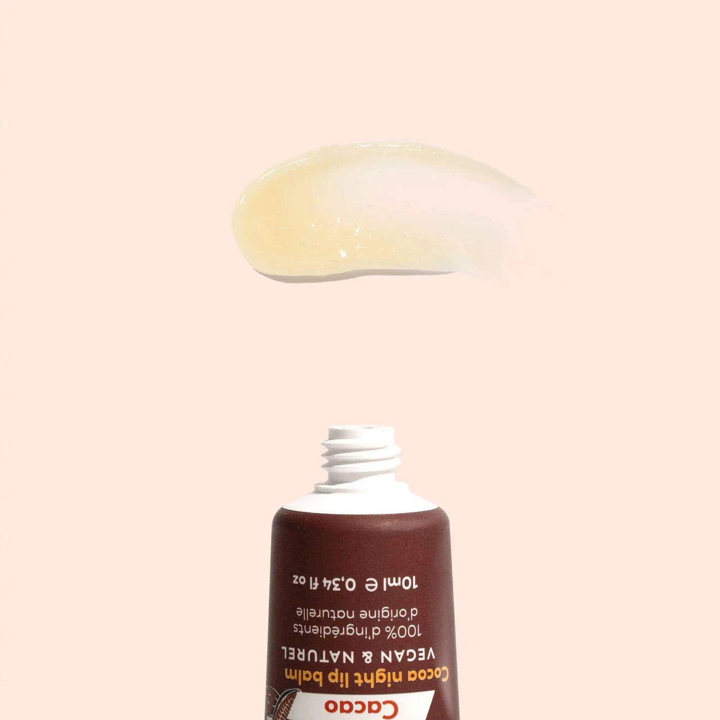 A swatch of translucent, pale yellow lip balm above an open, brown squeeze tube on a light peach background.