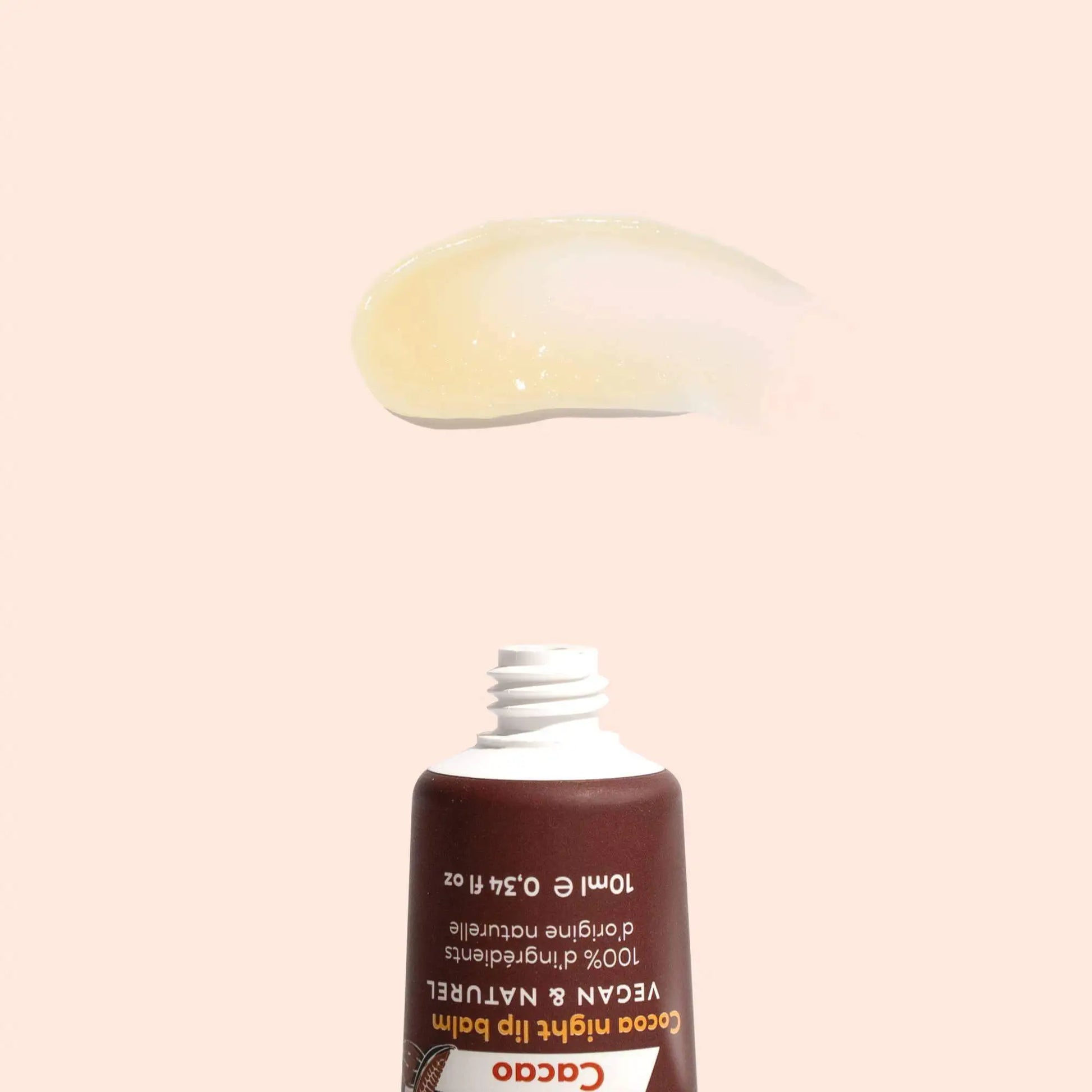 A swatch of translucent, pale yellow lip balm above an open, brown squeeze tube on a light peach background.