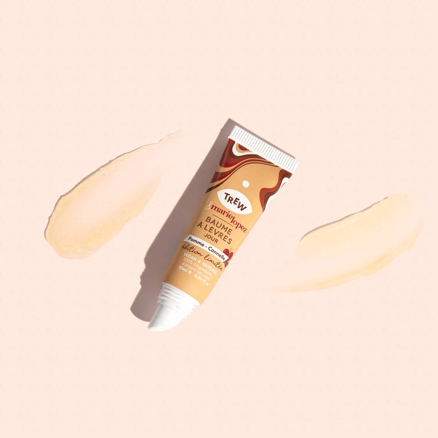 Lip balm tube with swirl design, labeled "Pomme Cannelle," centered between two sheer product swatches on beige.