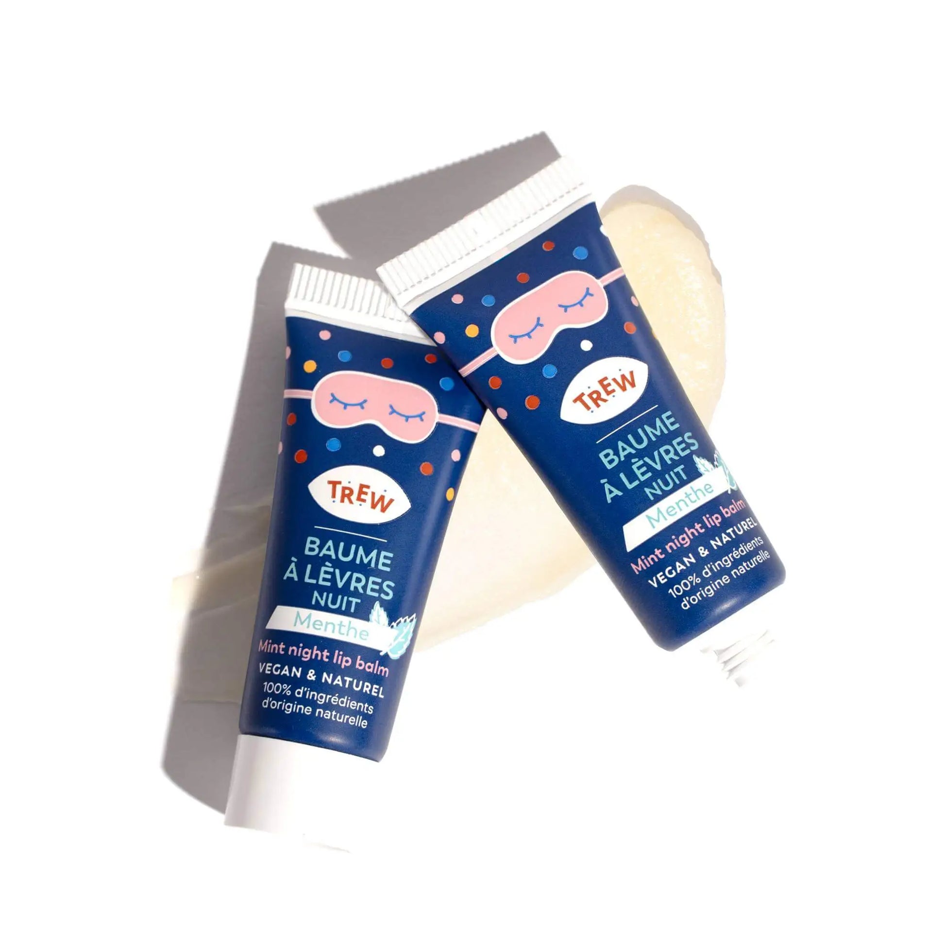 Deux tubes de baume à lèvres nuit Trew bleu marine à pois, avec une texture baume crémeuse translucide en arrière-plan.
