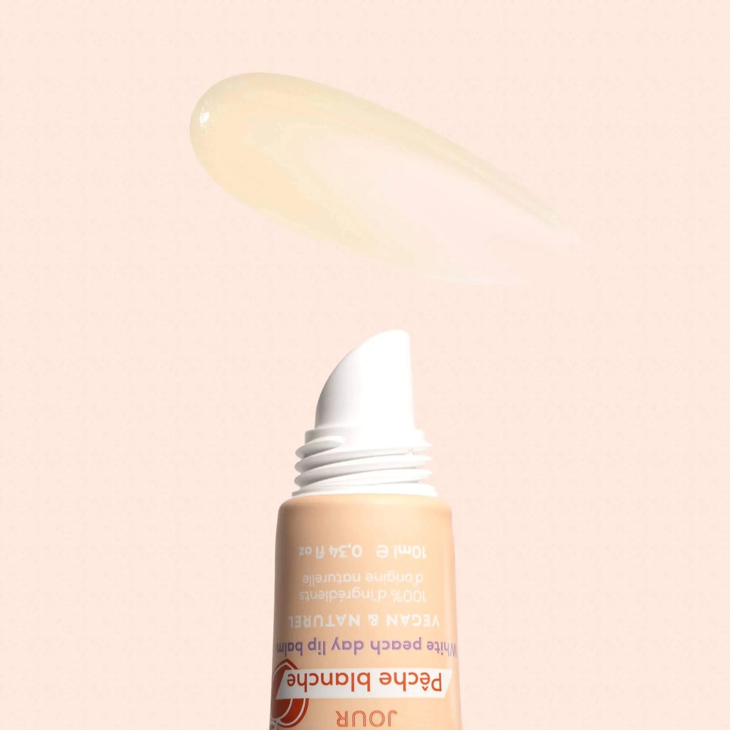 Squeeze tube of white peach lip balm with a smear of clear, glossy product above it on a soft peach background.