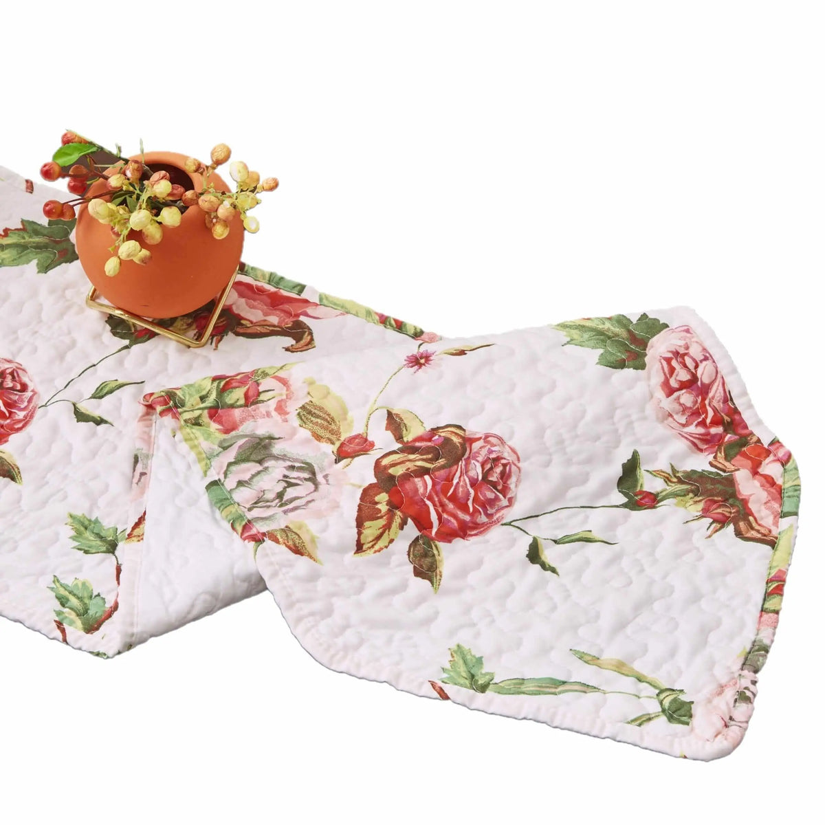 Quilted white dining table runner featuring pink and red rose floral patterns with green leaves and a small orange vase.