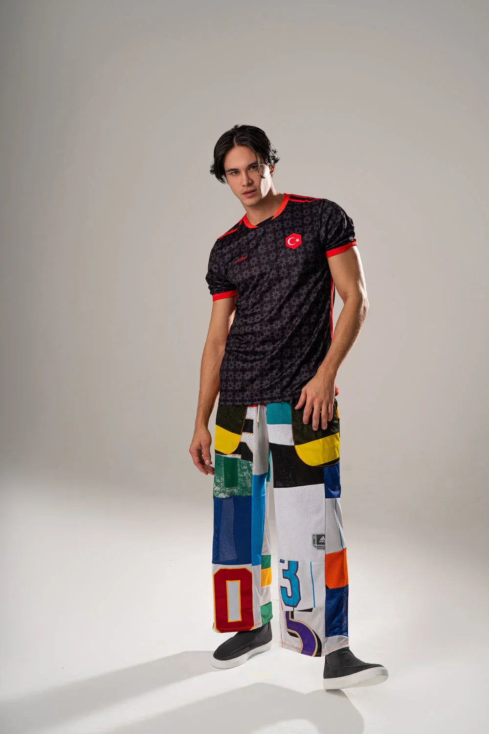 Maillot VO7 noir à motifs étoilés, détails rouges et blason de la Turquie, porté avec un pantalon multicolore en mesh.