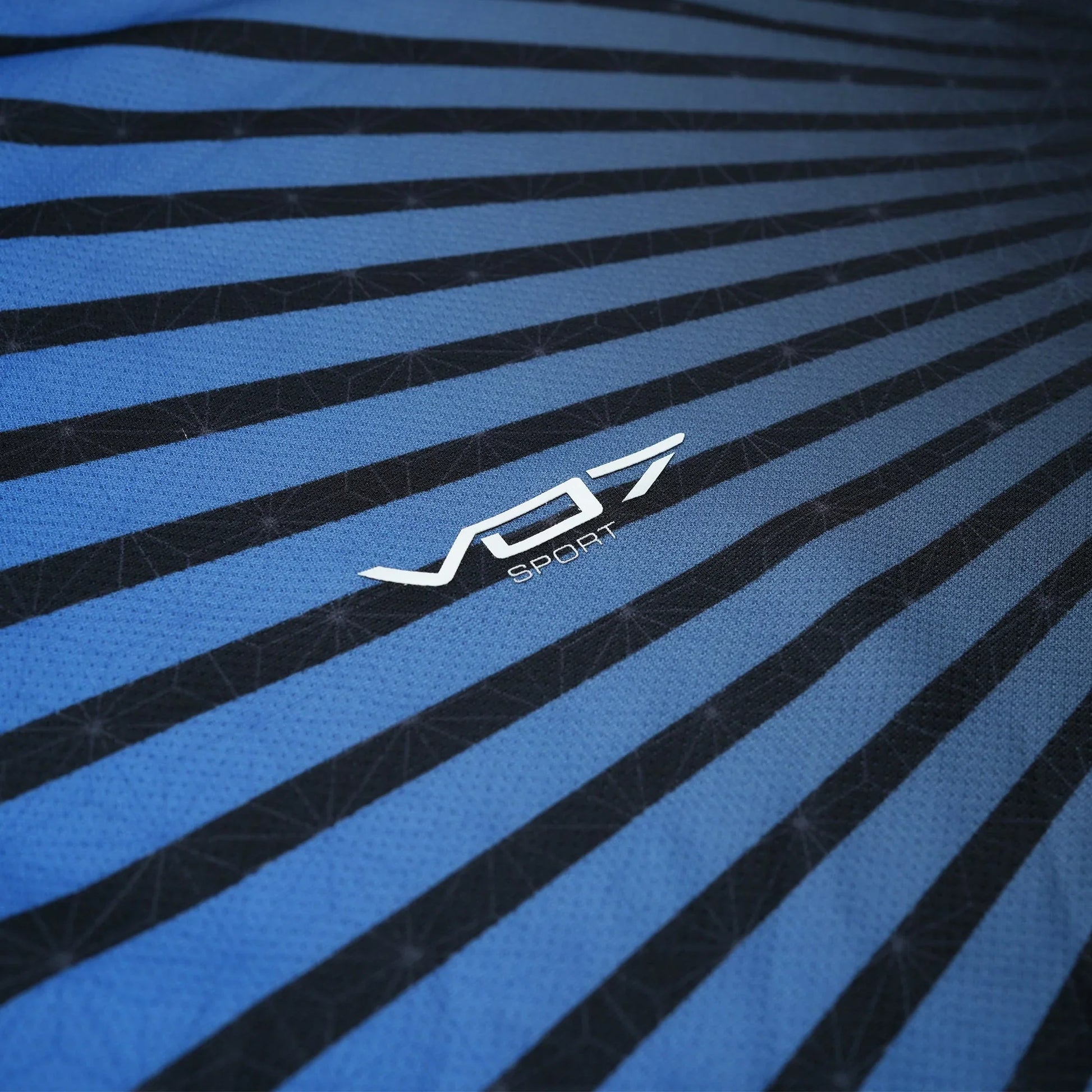 Maillot VO7 Sport bleu et noir à rayures, en matière technique respirante avec motif géométrique et logo blanc central.