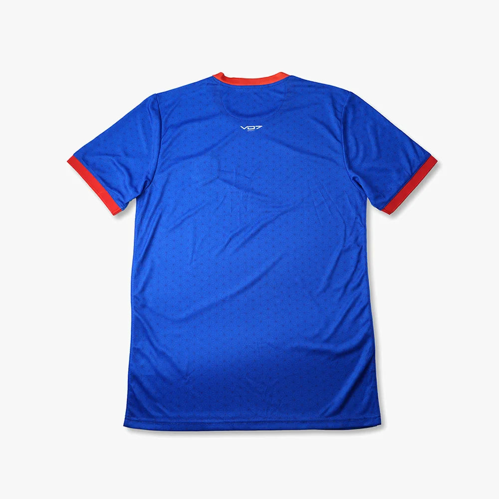 Maillot VO7 bleu à motif géométrique subtil, col et bords de manches contrastés rouge, logo blanc au niveau du col.
