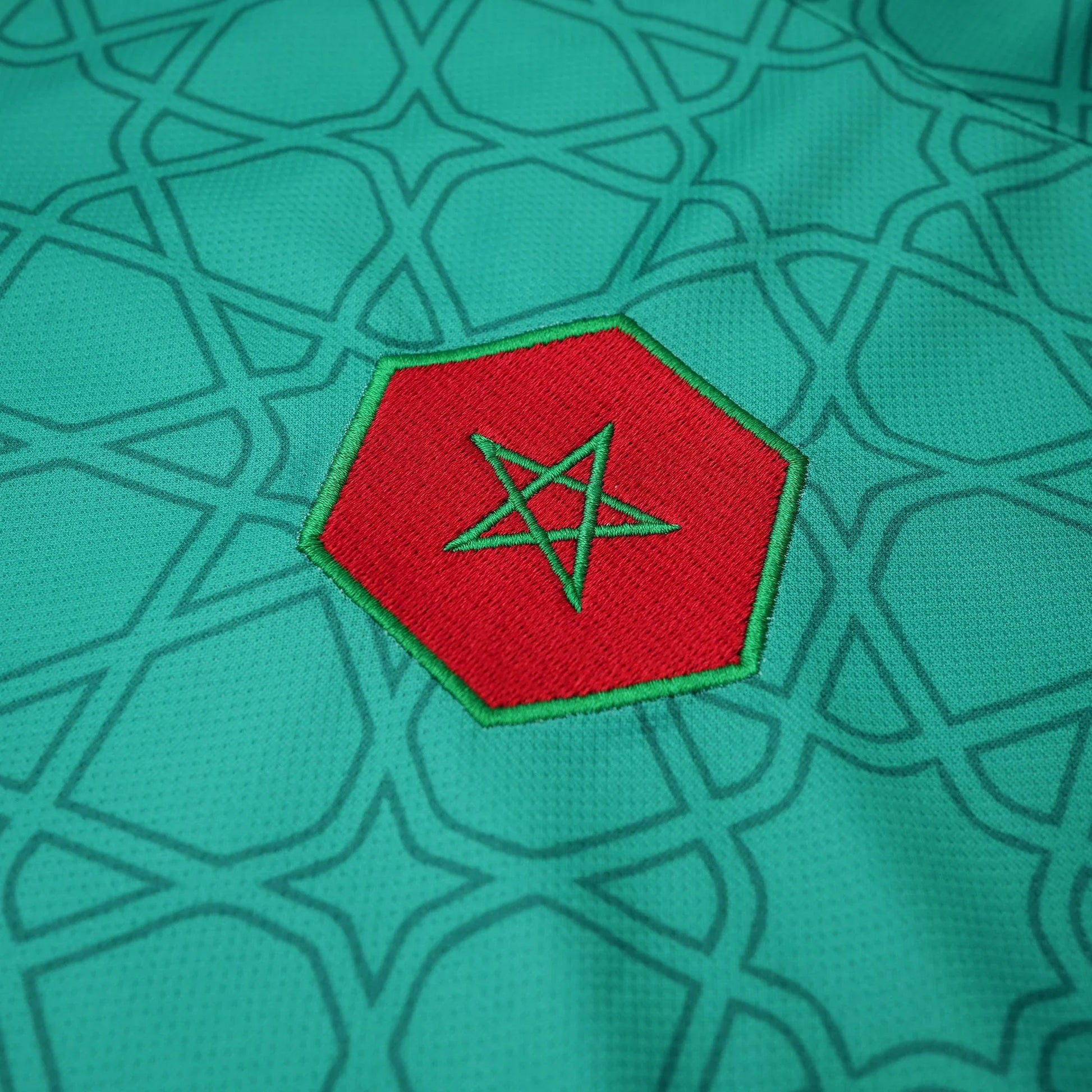 Maillot VO7 vert à motifs géométriques, avec un écusson hexagonal rouge brodé d'une étoile verte centrale.