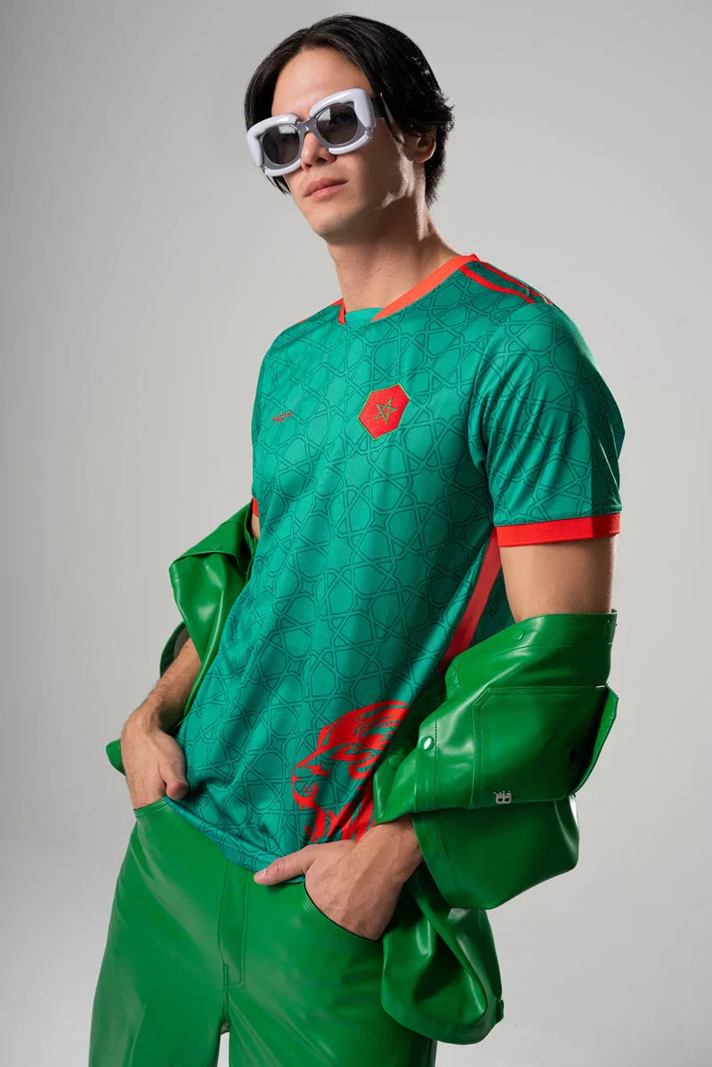Maillot VO7 vert à motifs géométriques, détails rouges, col rond et blason central sur homme portant une veste en cuir.