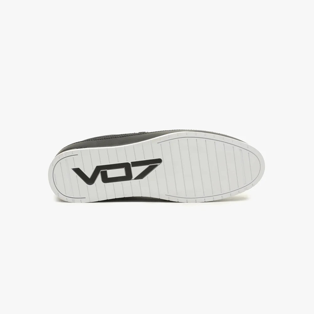 Semelle extérieure blanche striée d'une chaussure noire VO7, avec le logo noir marqué en relief au centre.